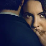 Ivana Baquero, atriz protagonista de "O Jogo da Viúva", em imagem de capa promocional para filme da Netflix. Ela está com o rosto encoberto pelos ombros de um homem, mão esquerda sobre ele, revelando a aliança, e um olhar enigmático. O homem está de terno e de costas.