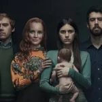 Quatro personagens da série "Servant" posando em família. A segunda mulher, ruiva, sorri, os demais membros da família estão com uma feição preta. O fundo é preto. A segunda mulher segura um bebê reborn desnudo virado com o lado do rosto para seu peito, apoiando seu colo e costas em sua mão.