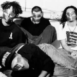 Membros do Rage Against The Machine sentados com braços para trás e fitas isolantes nos olhos e boca. Ensaio em preto e branco.