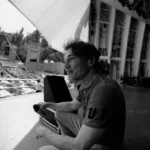 Vocalista do A-ha, Morten Harket, sentado em um palco de um show que ainda irá acontecer. Imagem em preto e branco. Ele sorri.