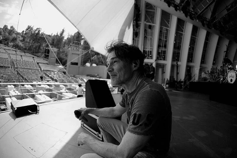 Vocalista do A-ha Revela Diagnóstico de Parkinson e Reflete Sobre Futuro na Música Vocalista do A-ha, Morten Harket, sentado em um palco de um show que ainda irá acontecer. Imagem em preto e branco. Ele sorri.