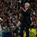 Técnico Carlo Ancelotti, ex-Real Madrid, de terno em um jogo do time. Ele está com uma expressão séria, batendo palmas, e podemos ver Federico Valverde à sua esquerda, parcialmente de costas e virado ao lado direito.