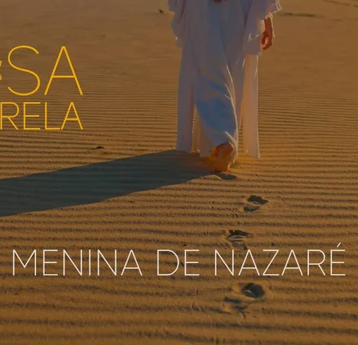 Capa do clipe "Menina de Nazaré", do duo Rosa Amarela. Pris Mariano, no lado direito do quadrante, quase ao meio, caminha nas areias e deixa pegadas. Está de dia e podemos ver sua sombra do lado esquerdo.