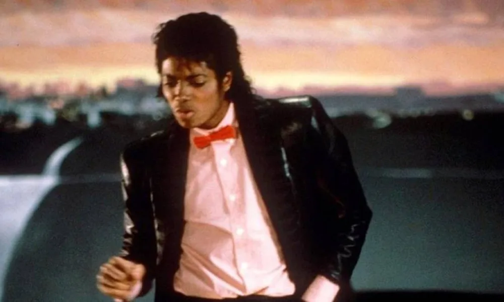 Michael Jackson em 1982 durante o clipe de "Billie Jean", dajçando com um cenário de pôr do sol ao fundo.