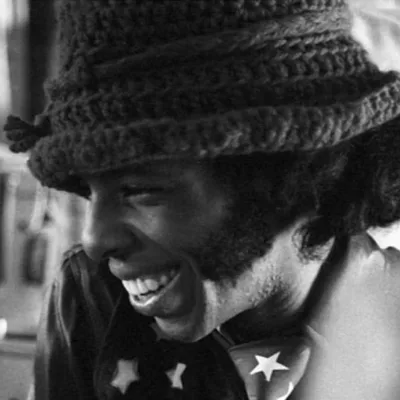 Sly Stone em foto preto e branco, sorrindo, de perfil, com uma toca de lã.
