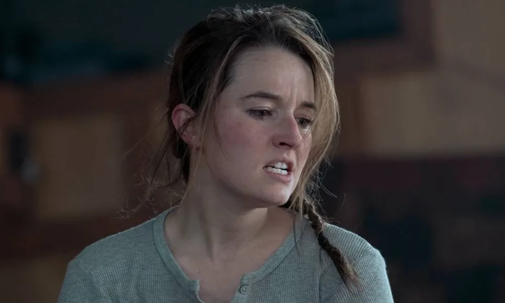 Kaitlyn Denver como Abby da série "The Last of Us". Cabelo bagunçado, boca aberta e dentes semicerrados, raiva, hesitação, sendo focada na tela.