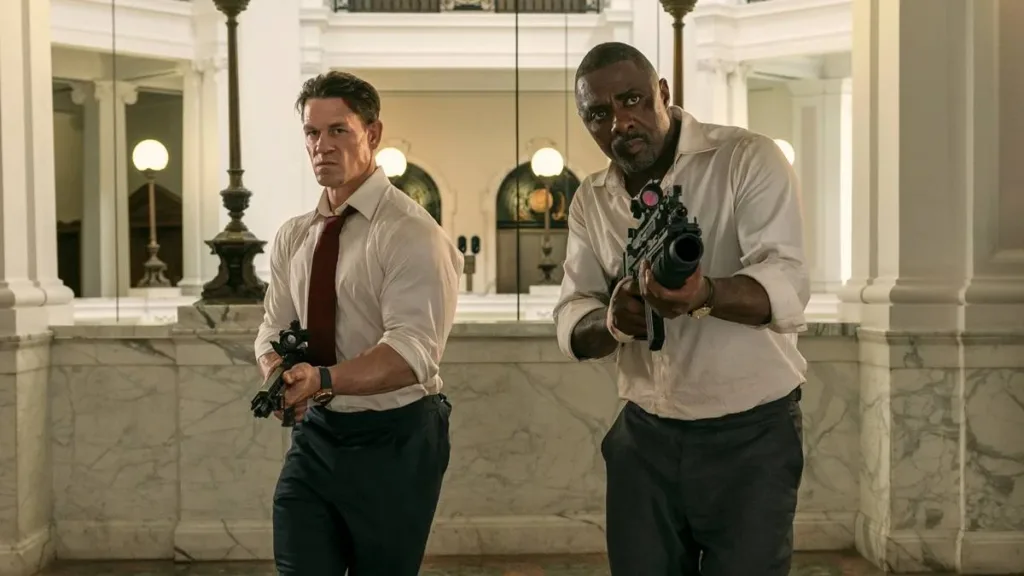 Chefes de Estado | Ação e Diversão Literalmente Em Dose Dupla 1 John Cena e Idris Elba em 'Chefes de Estado', interpretando o presidente dos EUA e primeiro-ministro da Inglaterra. Estão com camisa social e segurando metralhadoras.