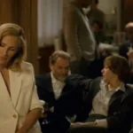 De branco, sentada no braço de um sofá, Julia Roberts é Alma Olsson, protagonista de "Depois da Caçada", em cena com encontro da alta sociedade no filme.