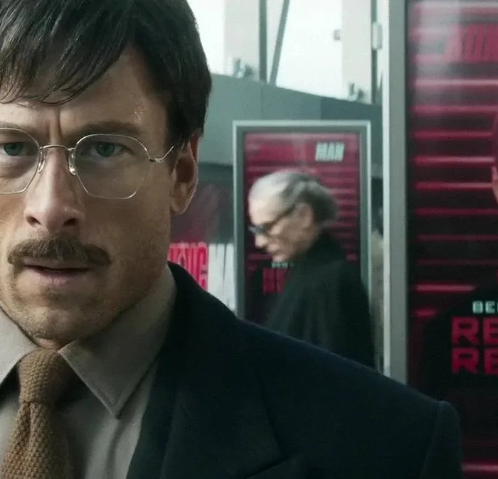 Glen Powell em "O Concorrente", remake de 2025. Ele está de terno e gravata, óculos e bigode, e uma expressão de angústia.