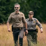 Quarteto Fantástico – Primeiros Passos | Nova Fase, Em Busca de Diferentes Resultados Eric Bana e Lily Santiago como Kyle Turner e Naya Vazques em meio a grama alta seca e vestidos como agentes na série da Netflix "Indomável".