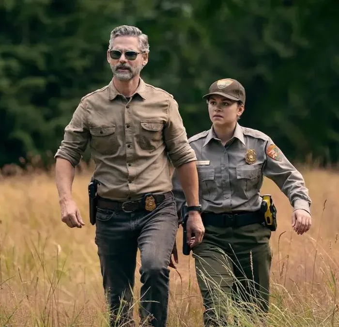 Eric Bana e Lily Santiago como Kyle Turner e Naya Vazques em meio a grama alta seca e vestidos como agentes na série da Netflix "Indomável".