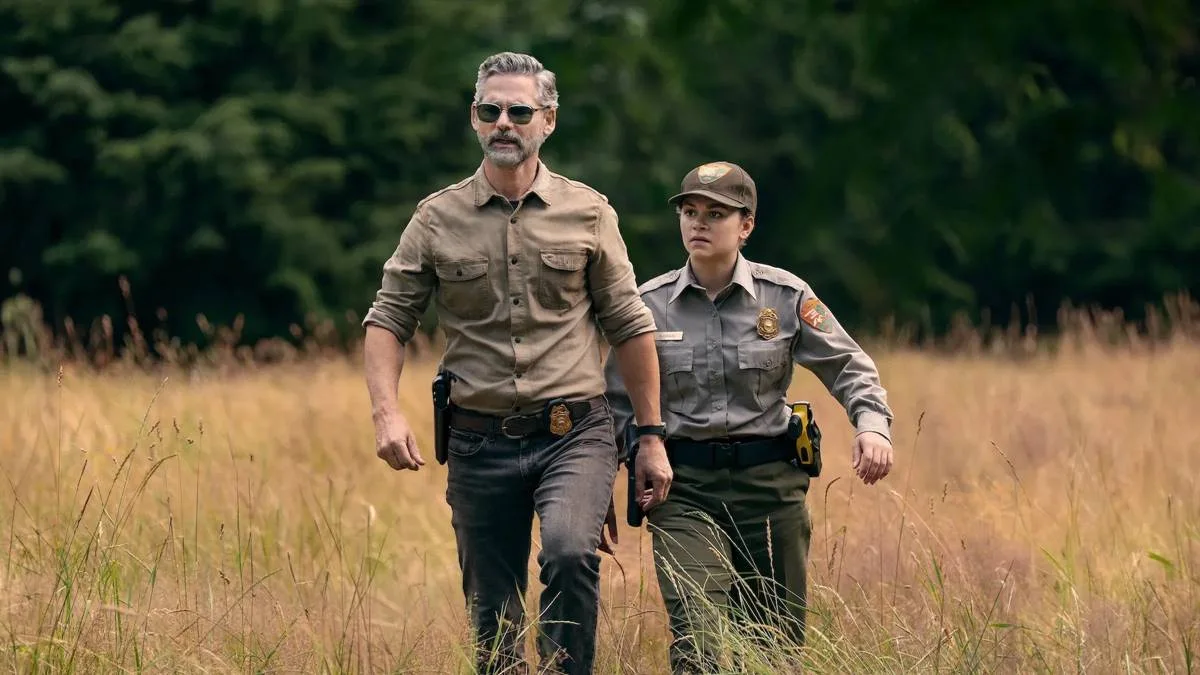 Indomável | O Trauma Como Motor de Nossas Ações 2 Eric Bana e Lily Santiago como Kyle Turner e Naya Vazques em meio a grama alta seca e vestidos como agentes na série da Netflix "Indomável".