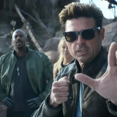 Karl Urban à direita em destaque, de óculos, como Johnny Cage no trailer de "Mortal Kombat 2", em posição de combate com a mão esquerda a frente do corpo.