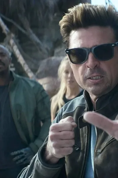 Karl Urban à direita em destaque, de óculos, como Johnny Cage no trailer de "Mortal Kombat 2", em posição de combate com a mão esquerda a frente do corpo.