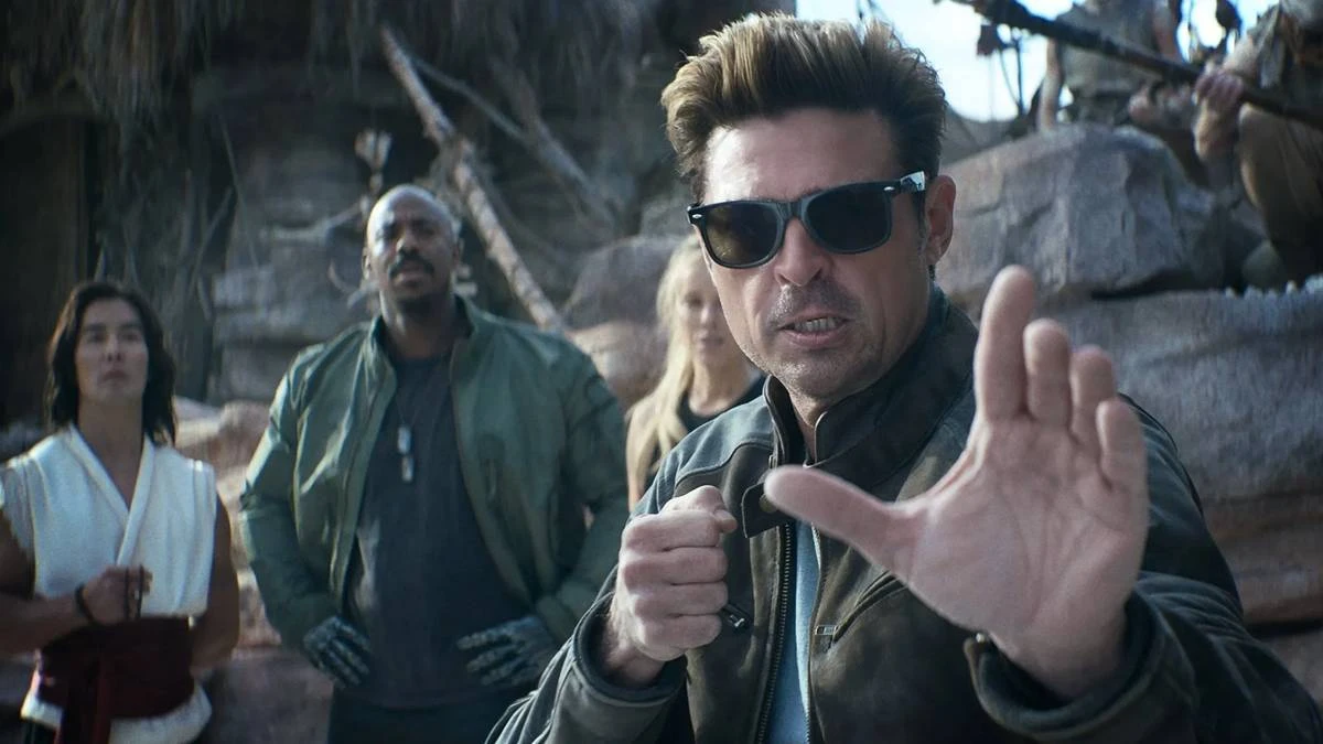 Karl Urban à direita em destaque, de óculos, como Johnny Cage no trailer de "Mortal Kombat 2", em posição de combate com a mão esquerda a frente do corpo.