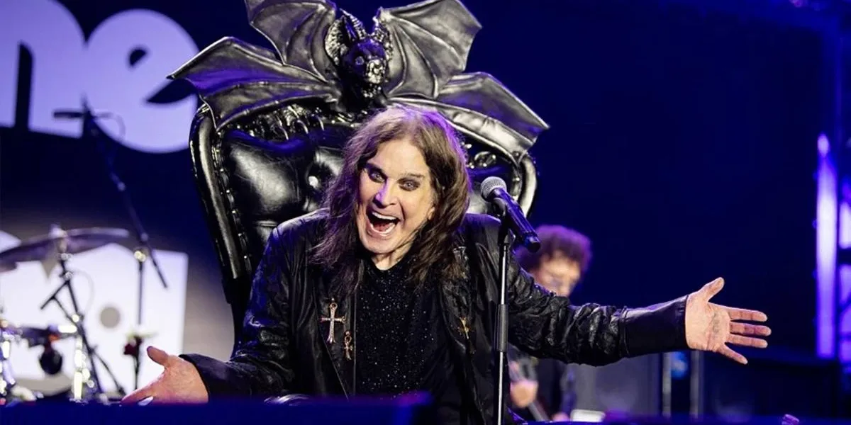 Ozzy Osbourne | Os 12 Clássicos mais Icônicos do Príncipe das Trevas Foto de Ozzy em trono negro adornado com um morcego, o vocalista de braços abertos sorrindo de boca aberta provocativamente, maquiagem forte, cabelos longos, em foto promocional para o "Back To The Beginning: Ozzy’s Final Bow", que será lançado em 2026.