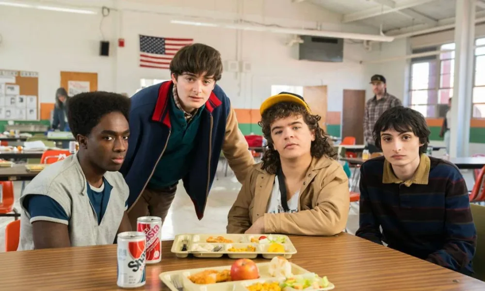 Caleb, Will, Dustin, Finn, em refeitório na quinta e última temporada de "Stranger Things", encarando a câmera.