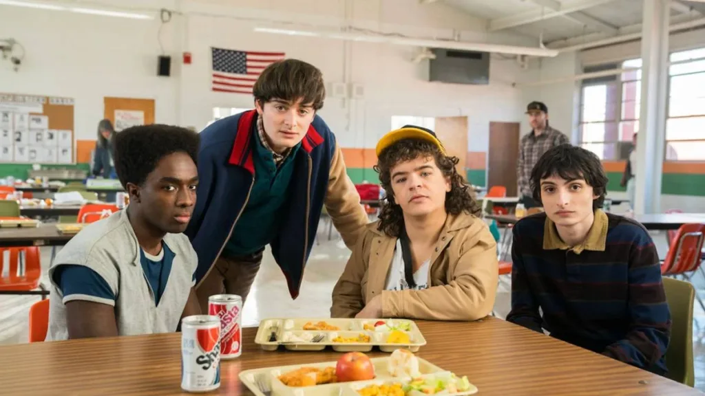 Stranger Things | A História de Hawkins, a Origem do Mundo Invertido e Tudo o Que Aconteceu Antes do Final 5 Caleb, Will, Dustin, Finn, em refeitório na quinta e última temporada de "Stranger Things", encarando a câmera.
