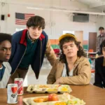 Caleb, Will, Dustin, Finn, em refeitório na quinta e última temporada de "Stranger Things", encarando a câmera.