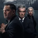 Tom Hardy a frente, de perfil, com Pierce Brosnan atrás e, por fim, Helen Mirren, matriarca da família, na série "Terra da Máfia". Palheta cinzenta, mas em cores, com uma casa cinza ao fundo e um gramado verde triste.