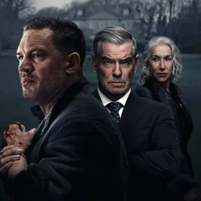 Tom Hardy a frente, de perfil, com Pierce Brosnan atrás e, por fim, Helen Mirren, matriarca da família, na série "Terra da Máfia". Palheta cinzenta, mas em cores, com uma casa cinza ao fundo e um gramado verde triste.