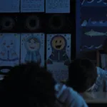 Crianças em sala de aula em "A Hora do Mal", de cabeça para baixo. Um garoto, ao fundo, é o único de cabeça erguida, com um sorriso desconcertante e maquiagem à Coringa.