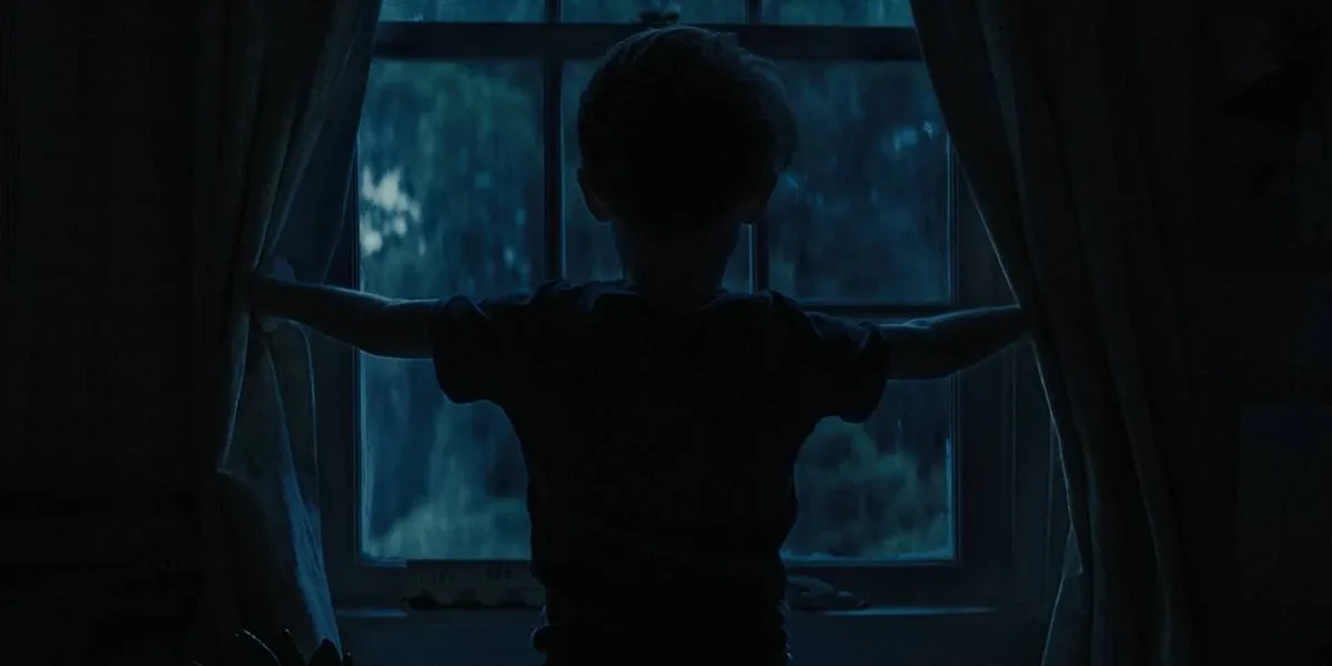A Hora do Mal | Terror Grotesco Com Julia Garner e Josh Brolin Prende do Início ao Fim Criança de "A Hora do Mal" vista apenas por sua silhueta preta abrindo uma janela de noite, de costas.