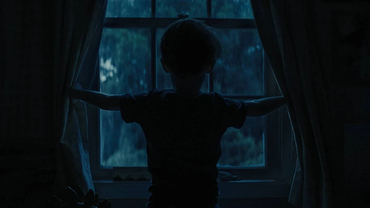 A Hora do Mal | Terror Grotesco Com Julia Garner e Josh Brolin Prende do Início ao Fim 2 Criança de "A Hora do Mal" vista apenas por sua silhueta preta abrindo uma janela de noite, de costas.