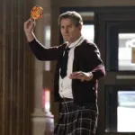 Liam Neeson vestindo kilt, roupa social e gravata, empunhando um pirulito gigante colorido como se fosse uma arma de arremesso no reboot de 2025 de "Corra Que a Polícia Vem Aí".