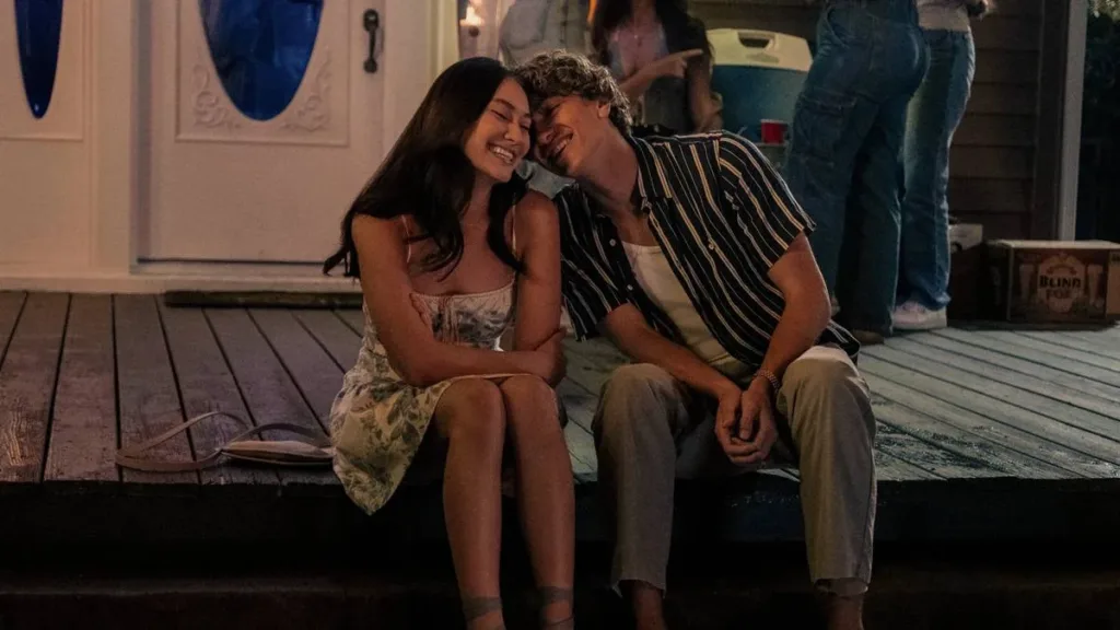 O Verão Que Mudou Minha Vida | Série da Prime Video Conquista Jovens ao Redor do Mundo 1 Belly à esquerda e Jeremiah à direita, inclinando-se afetivamente perto da nuca de Belly, ambos rindo em uma cena noturna com ambos sentados em um cais de madeira. Imagem da série "O Verão Que Mudou Minha Vida".