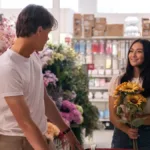 Conrad, de costas, virado à Belly, em 'O Verão Que Mudou Minha Vida', adaptação em série da Prime Video. Ela segura girassóis em uma floricultura.