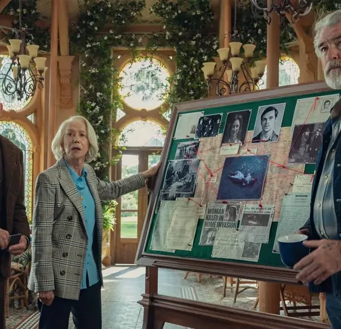 Na esquerda e mais ao fundo: Ben Kingsley e Helen Mirren, que segura o quadro, e à direita do quadro e mais à frente Pierce Brosnan. Atores interpretam seus personagens em "O Clube do Crime das Quintas-feiras", da Netflix, e estão ao lado de um quadro verde com mapa mental para resolução criminal, cheio de colagens, e olham para um mesmo ponto do outro lado da tela.