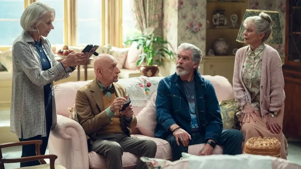 O Clube do Crime das Quintas-feiras | Mais Um Filme da Netflix, Dessa Vez Com Um Elenco Estelar 1 Da esquerda para a direita: Helen Mirren em pé segurando seu celular, Ben Kingsley e Pierce Brosnan sentados no sofá, e Celia Imrie sentada no braço do sofá. Atores interpretam seus papéis no filme "The Thursday Murder Club" da Netflix.