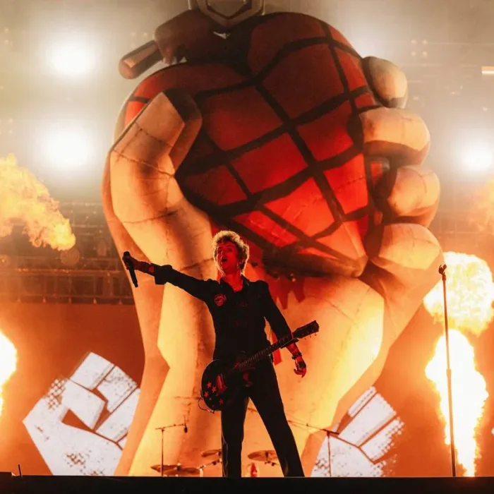 Billie Joe Armstrong com mão direita levantada com microfone à plateia, em foto centralizado no palco Skyline do The Town 2025. Ao fundo há pirotecnia e uma representação da capa do álbum American Idiot esculpida.