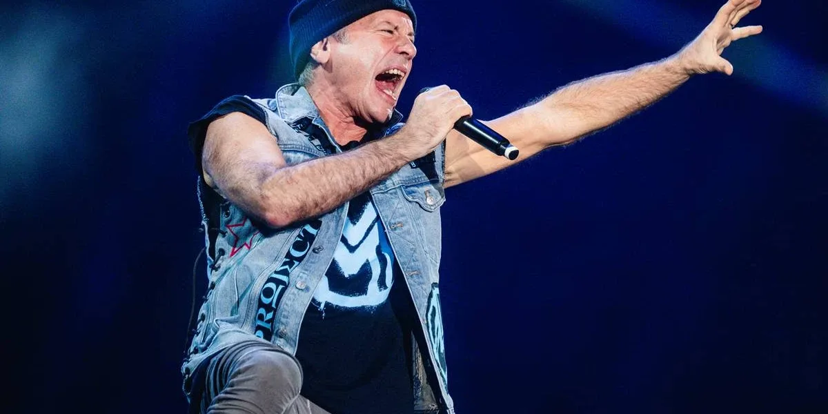 The Town 2025 | Bruce Dickinson Mostra Por Que Não Precisa do Iron Maiden Bruce Dickinson, jaqueta de couro, touca preta, segurando microfone na mão direita e com a mão direita estendida e aberta em garra, cantando com boca bem aberta em foto em seu show no Palco Skyline no The Town 2025.