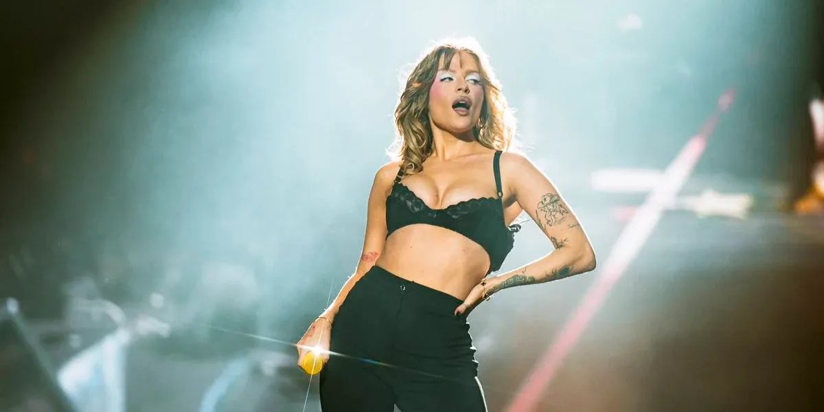 The Town 2025 | Luísa Sonza Traz Repertório Com Covers e Preludia Novo Álbum Luisa Sonza no palco The One do The Town 2025. Ela está com mão na cintura, vestindo jeans e sutiã pretos, meio inclinada para sua esquerda, segurando o microfone na mão direita e de boca aberta. Está com maquiagem forte, pegada no blush e com azul forte ao redor dos olhos.