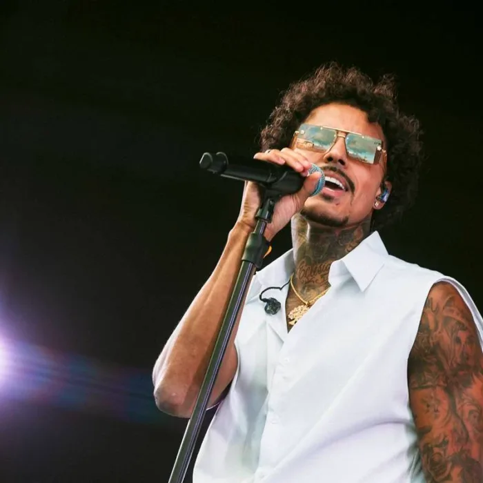 Livinho com um colete branco, segurando o microfone com a mão direita, e rosto levemente inclinado no sentido oposto, de óculos no palco Factory do sábado do The Town 2025.