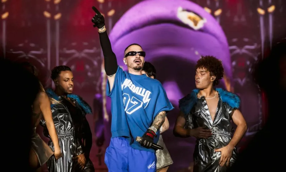 J Balvin, camiseta e calça azul, luva preta na mão estendida, óculos escuros, em apresentação no The Town 2025.