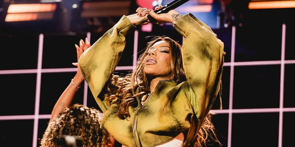 Ludmilla de olhos fechados, microfone na mão esquerda, e braços estendidos ao alto semidobrados, em show no The Town 2025.