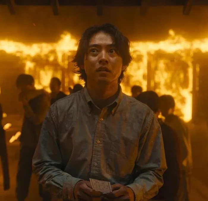 Arisu no segundo episódio da terceira temporada de "Alice in Borderland". Roupa social, no meio de uma multidão em um ambiente em chamas.