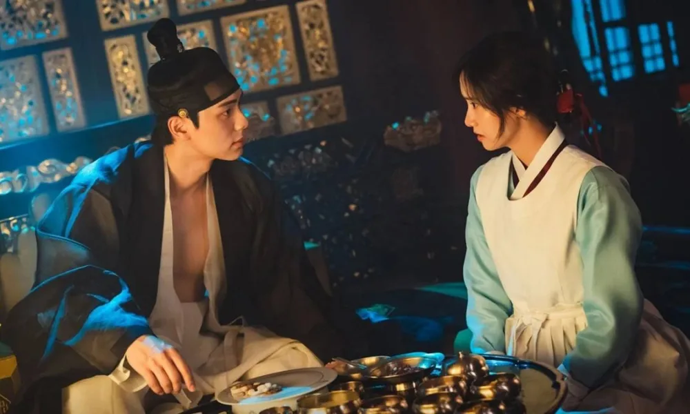 Lee Chae-min e Yoona como os protagonistas de "Bon Appétit, Vossa Majestade". Ele está com as roupas de rei de Joseon, Yi Heon, olhando para ela e vice-versa, e Yoona é Yeon Ji-young, cozinheira chefe real.
