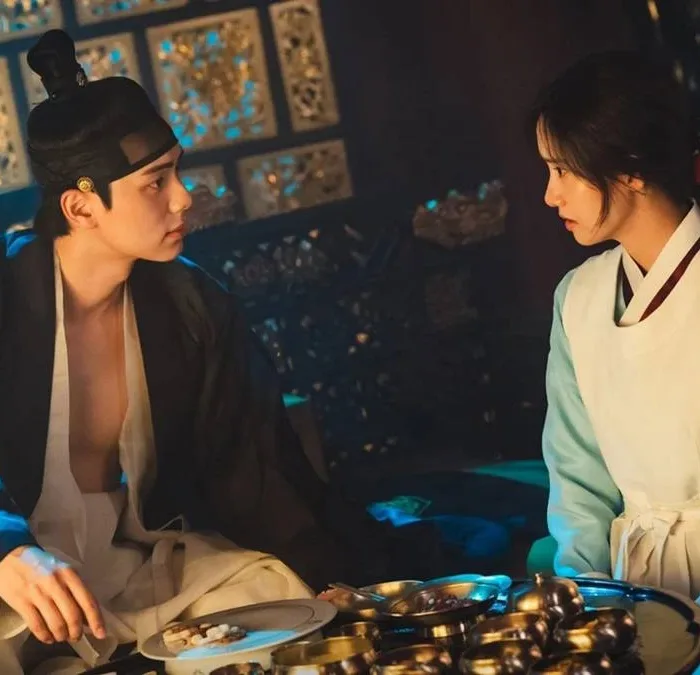 Lee Chae-min e Yoona como os protagonistas de "Bon Appétit, Vossa Majestade". Ele está com as roupas de rei de Joseon, Yi Heon, olhando para ela e vice-versa, e Yoona é Yeon Ji-young, cozinheira chefe real.