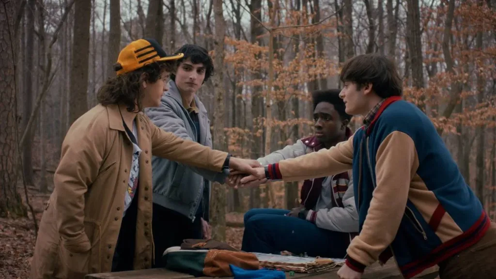 Emmy Awards: curiosidades sobre a maior premiação da TV e os destaques da edição de 2026 3 Os quatro protagonistas masculinos de Stranger Things dando as mãos em uma rodinha no primeiro episódio da última temporada, em um bosque que parece estar no outono.