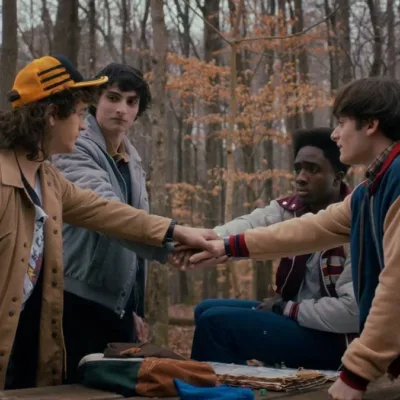 Stranger Things | Última Temporada Tem Convite dos Astros Aos Fãs Os quatro protagonistas masculinos de Stranger Things dando as mãos em uma rodinha no primeiro episódio da última temporada, em um bosque que parece estar no outono.
