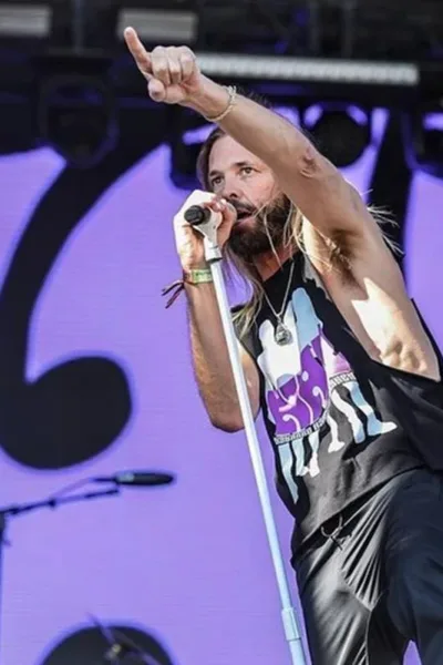 Amante Declarado de Prog Rock, Taylor Hawkins foi Repreendido Pelos Integrantes do Rush Taylor Hawkins em ângulo plongée, de regata preta e jeans, apontando com o indicador para a plateia com o braço direito levantado e o esquero segurando o microfone em apresentação.