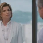 Débora Bloch como Odete Roitman em Vale Tudo, de roupa social branca, encarando irritada Marco Aurélio (Alexandre Nero) que está de costas para a tela, de frente para nós.