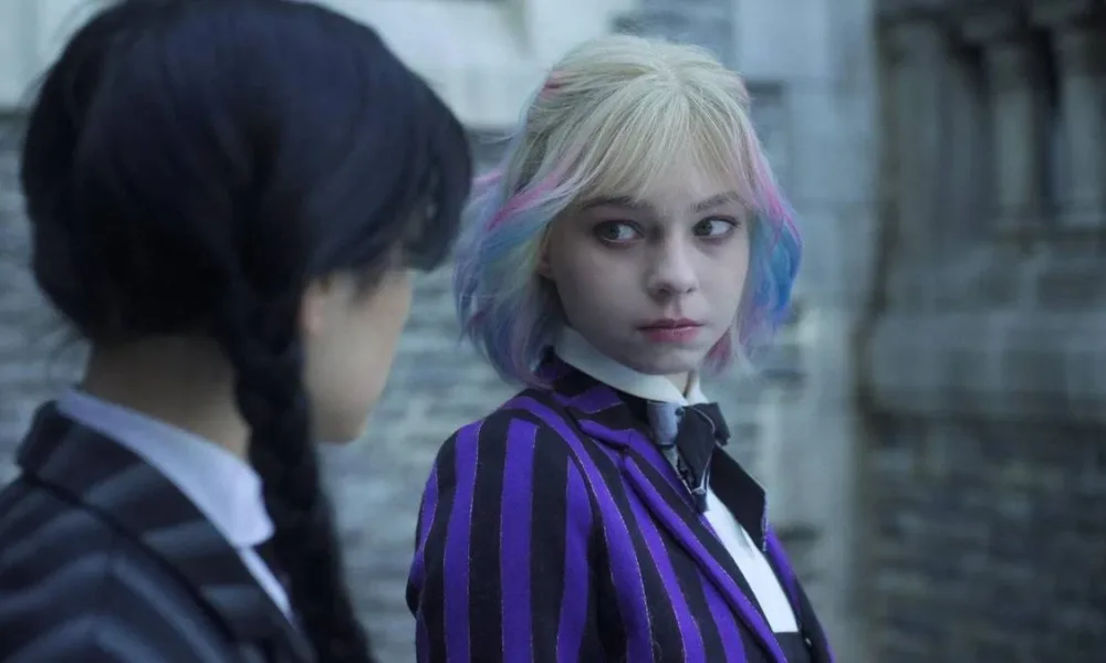 Jenna Ortega de lado como Wandinha, e Emma Myers sutilmente virada para o lado com o uniforme de Nunca Mais, encarando-a, como a personagem Enid Sinclair. Wandinha e Enid estão com corpos trocados, razão pela qual Enid é na verdade Wandinha e está a encarando profundamente.