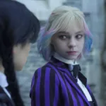 Jenna Ortega de lado como Wandinha, e Emma Myers sutilmente virada para o lado com o uniforme de Nunca Mais, encarando-a, como a personagem Enid Sinclair. Wandinha e Enid estão com corpos trocados, razão pela qual Enid é na verdade Wandinha e está a encarando profundamente.