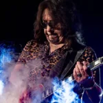 Ac Frehley tocando guitarra em show em 2025. Fumaça de glicerina pode ser vista no palco, ele com um semblante concentrado.