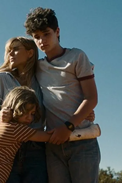 Pequenas Criaturas | Conheça o Filme Vencedor do Troféu Redentor de Melhor Longa de Ficção da Première Brasil Helena (Carolina Dieckmann) e seus filhos, André (Théo Medon) e Dudu (Lorenzo Mello) no filme "Pequenas Criaturas", todos abraçados em um céu azul com filtro que dá a impressão de um Brasil dos anos 80.